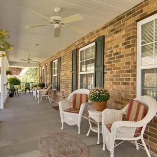 A cozy porch featuring wicker chairs and potted plants against a brick wall.