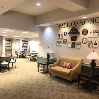 A comfortable lounge area featuring a 'Wall of Honor' adorned with plaques and awards, along with seating options including sofas, tables, and chairs.