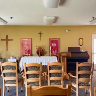 View of a small chapel with an altar, chairs, and a cross on the wall.