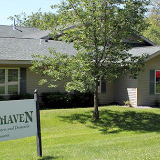 A suburban house with a sign in the yard reading 'Haven', surrounded by trees and grass.