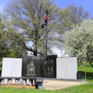An outdoor memorial monument with engraved images and a flag on a sunny day.