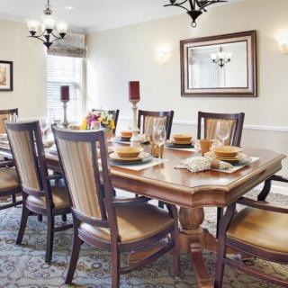 A traditional dining room with a large wooden table set for a meal, surrounded by cushioned chairs and adorned with elegant lighting.