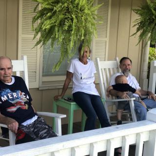 A group of people relaxing on a porch with rocking chairs and ferns.