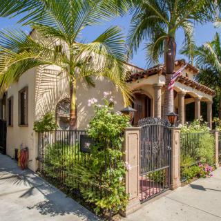 A charming house with a gated garden and lush palm trees basking in the sun.