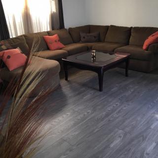 A cozy living room featuring a large sectional sofa with colorful pillows and a dark coffee table on wooden flooring.