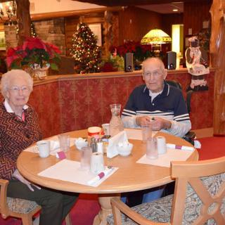 An elderly couple sitting at a table in a restaurant decorated for Christmas.