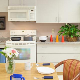 A cozy kitchen with a stove, microwave, and dining table featuring flowers and cookware.
