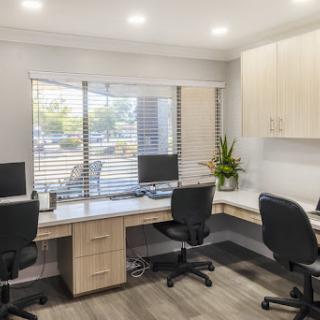 A modern office workspace featuring two desks equipped with computers and ergonomic chairs, illuminated by natural light.