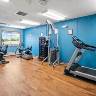 A modern fitness center with various exercise equipment, including a treadmill and elliptical machine, featuring blue walls and wooden flooring.