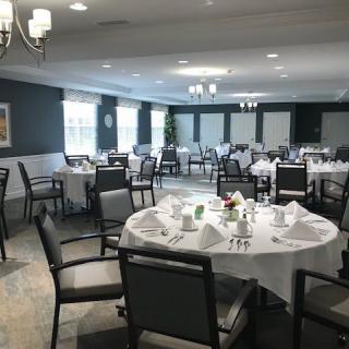 An elegantly set dining room with round tables and chairs arranged for a formal event.