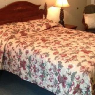 A cozy bedroom featuring a bed with a floral bedspread, accompanied by a bedside lamp and an upholstered chair.