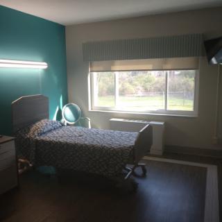 A well-lit hospital room featuring a single bed and a view out the window.