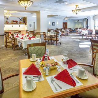 A spacious dining room with elegantly set tables, featuring red napkins and fine tableware.
