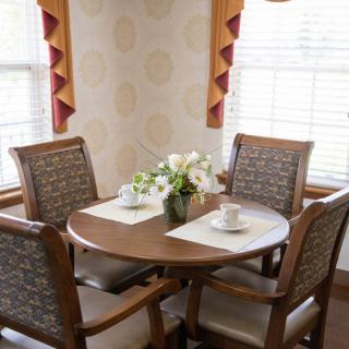 A cozy dining area with a wooden table, four chairs, and a floral centerpiece by a window with curtains.
