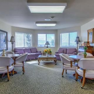 A cozy living room with sofas and tables arranged around a central area, featuring large windows and soft lighting.