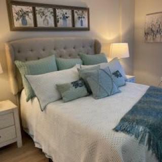 A cozy bedroom with a neatly made bed, featuring multiple pillows and teal accents.