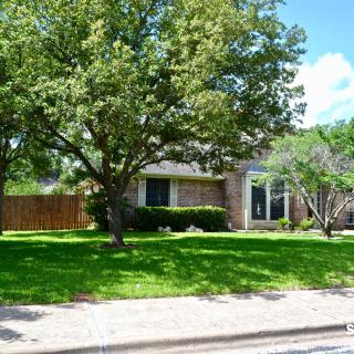 A suburban house with a large tree and green lawn in the front yard.