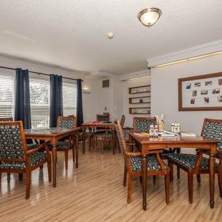 A cozy dining area with neatly arranged tables and chairs, featuring large windows and wooden flooring.