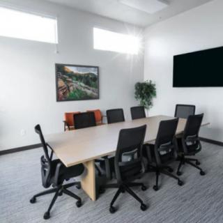 A modern conference room with a long meeting table and several chairs, featuring wall art and a television screen.