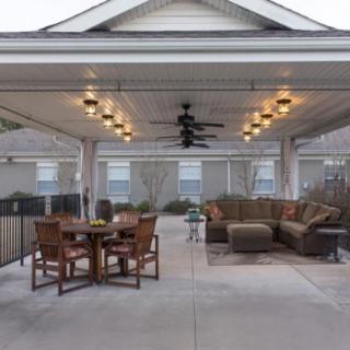 A spacious covered patio featuring a dining table and a cozy sofa set under warm lighting.