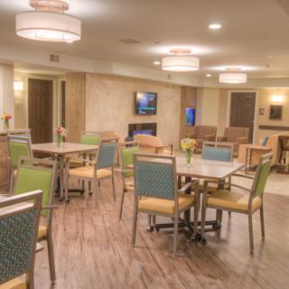 A modern dining area with tables and chairs, featuring soft lighting and a TV screen on the wall.