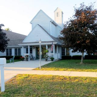 A white church building with a steeple surrounded by trees and a sidewalk.