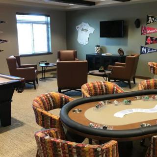 A stylish game room featuring a poker table, pool table, and cozy seating area with sports decorations on the walls.