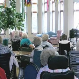 A group of elderly individuals seated in wheelchairs inside a care facility.