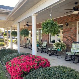 A cozy porch with rocking chairs and hanging plants, surrounded by colorful flowers.