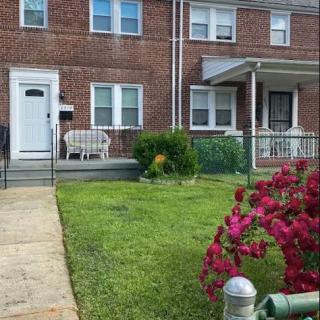 A charming brick house with a well-maintained front yard, featuring a lush green lawn and vibrant flowers along the path.
