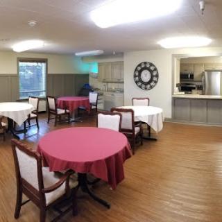 A cozy dining area with red tablecloths, featuring wooden flooring and a view of the kitchen.