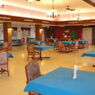 An empty dining room with tables covered in blue tablecloths, arranged neatly with chairs around them.