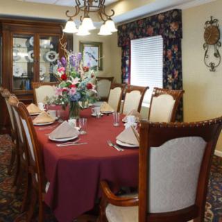 An elegant dining room set with a red tablecloth and floral centerpiece, surrounded by wooden chairs.