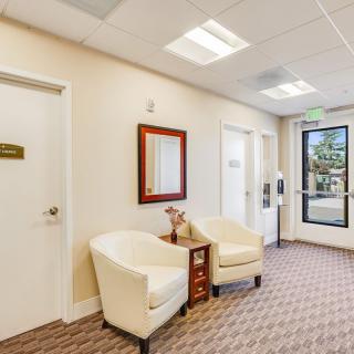 A cozy waiting room featuring two white chairs, a mirror, and soft lighting.