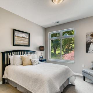 A cozy bedroom with a neatly made bed, decorated with pillows and framed artwork on the walls, featuring a window letting in natural light.