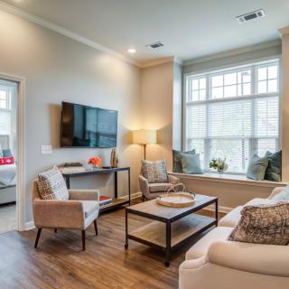 A cozy and modern living room with stylish furniture, a mounted TV, and large windows allowing natural light.