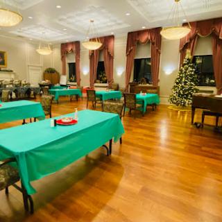A cozy dining room set up for a festive gathering, featuring green tablecloths and a Christmas tree.