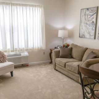 A cozy living room with a beige sofa, white chair, lamp, and artwork on the wall.