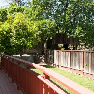 A wooden deck overlooking a fenced yard with lush green trees.