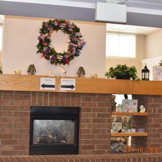 A cozy living room with a brick fireplace, adorned with a floral wreath and decorative items on shelves.