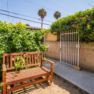 A sunny garden scene with a wooden bench, lush greenery, and a gated pathway.