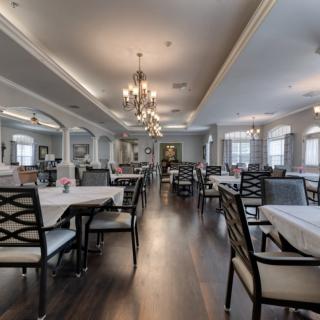 An elegant dining area with neatly arranged tables, chairs, and chandeliers under warm, bright lighting.