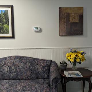 A cozy living room corner featuring a patterned couch, decorative artwork on the wall, and a vibrant bouquet of flowers on a side table.