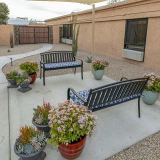 An outdoor patio area with benches and potted plants, surrounded by a garden courtyard.