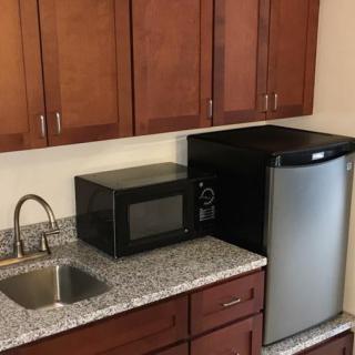 Small kitchen area with wooden cabinets, a microwave, a sink, and a mini fridge.