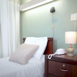 A clean and organized hospital room with a bed, nightstand, lamp, and phone.