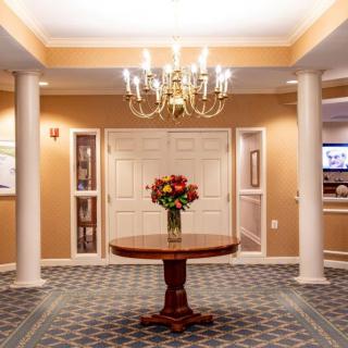 A spacious lobby with elegant decor, featuring a central table adorned with flowers and a chandelier above.