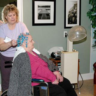 An older woman gets her hair styled with perm rods at a hair salon.