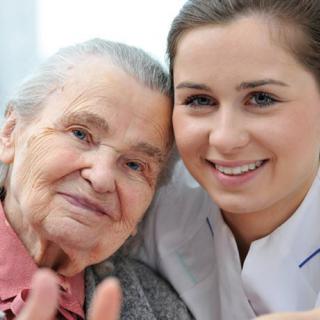 A caregiver embracing an elderly woman, both smiling warmly.