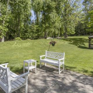 A peaceful garden patio with white outdoor benches, surrounded by lush greenery on a sunny day.